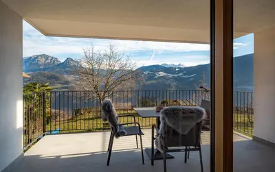 a balcony with a table and chairs and mountains at Gestüt Feuerstein- Lanznasterhof in Prato allʼIsarco
