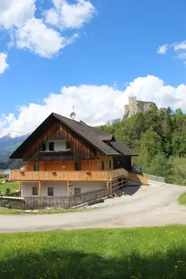 a large wooden building with a castle in the background at Oberkrösserhof in San Lorenzo di Sebato