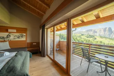 a bedroom with a balcony with a bed and a table at Berghotel Zorzi in Alpe di Siusi