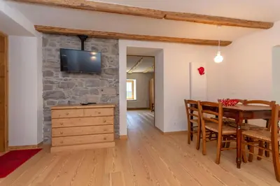 a dining room and living room with a stone wall at Appartamento Focobon in Falcade