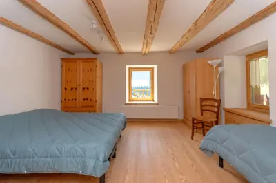 a bedroom with two beds and a chair and a window at Appartamento Focobon in Falcade
