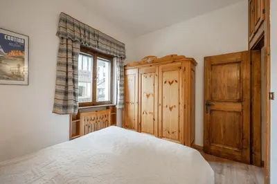 a bedroom with a bed and a wooden cabinet and a window at Lovely 2 bedroom flat in Corso Italia with parking in Cortina dʼAmpezzo