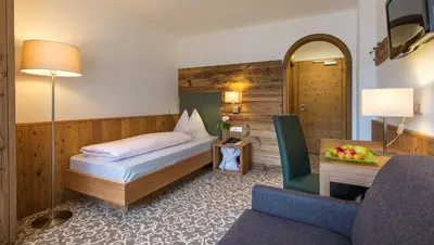 a hotel room with a bed and a chair at Garni Jasmin in Kastelruth