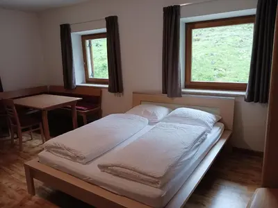 a bedroom with two beds and a table and two windows at Gasthof Alpenrose - Mühleben in Sarntal