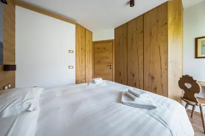 a bedroom with a white bed with a wooden wall at Chalet Belvedere - Dolomiti Skyline in Cortina dʼAmpezzo