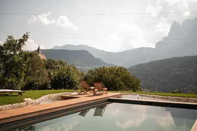 a pool with two chairs and a view of mountains at Hofgut Antlas in Collalbo