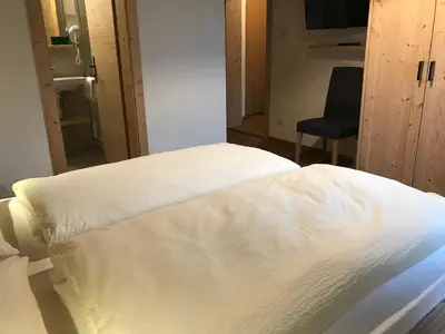 a white bed in a room with a chair at Platzerhof in Monguelfo