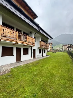 a building with wooden balconies and a grass yard at Appartamento Larsech in Pozza di Fassa