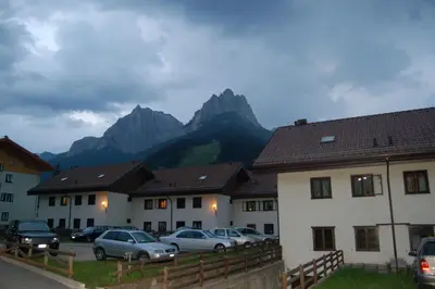 a group of buildings with cars parked in front of mountains at Appartamento Larsech in Pozza di Fassa