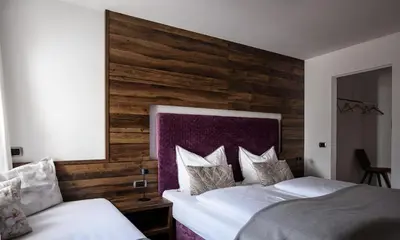 a bedroom with two beds and a wooden wall at La Funtana in Santa Cristina in Val Gardena