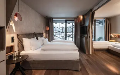 a bedroom with two beds and a table and a window at Falkensteiner Family Resort Lido l 4 Star Superior in Chienes
