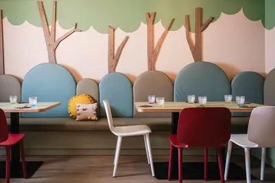 a dining room with tables and chairs and trees painted on the wall at Falkensteiner Family Resort Lido l 4 Star Superior in Chienes