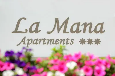 a sign for la manana apartments above flowers at Apartments La Mana in Santa Cristina in Val Gardena