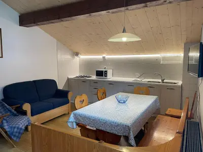 a living room with a table and a kitchen at Mansarda Mulaz in Falcade