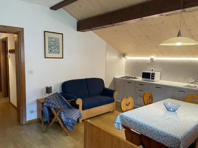 a living room with a blue chair and a kitchen at Mansarda Mulaz in Falcade