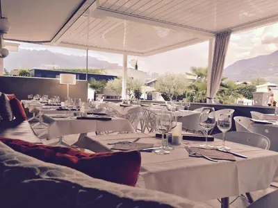 a restaurant with white tables and white chairs and windows at SCHLOSSHOF SÜDTIROL - Hotel & Camping Resort in Lana