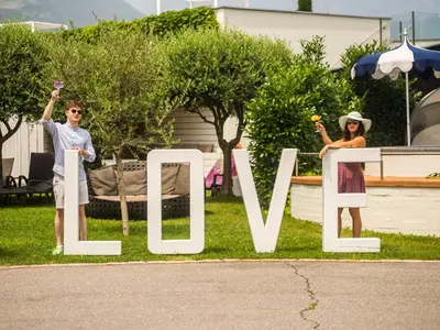 a man and woman standing next to a sign that reads wine at SCHLOSSHOF SÜDTIROL - Hotel & Camping Resort in Lana
