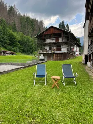 two chairs and a table in the grass in front of a building at Stella Alpina - Romantic getaway in Falcade