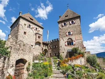 two towers of a building with flowers on a hill at Janas Bolzano Mountain Apartment in Tesimo
