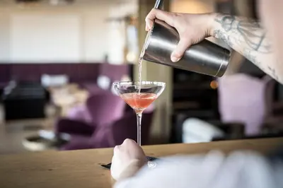a person pouring a drink into a cocktail glass at Served Apartements Belvedere in San Genesio Atesino