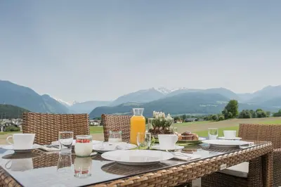 a table with food and drinks on a patio with mountains at Hotel Garni Hochgruber in Brunico
