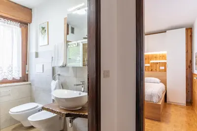 a bathroom with a sink and a toilet and a bed at Bilo Cornetto Bianco in Predazzo