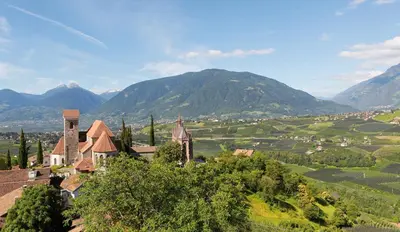 a church on a hill with mountains in the background at Family Hotel Gutenberg in Schenna