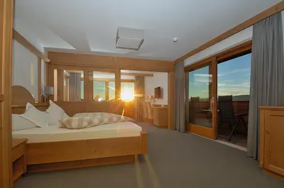 a bedroom with a bed with the sun shining through the windows at Hotel Rosslaufhof in Castelrotto