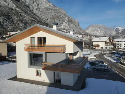 a house with a balcony with mountains in the background at Appartamento Miele di Pino in Ziano di Fiemme