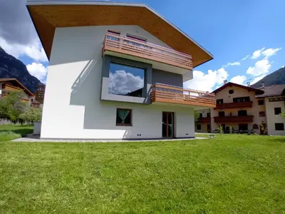 a house with a large window and a green yard at Appartamento Miele di Pino in Ziano di Fiemme
