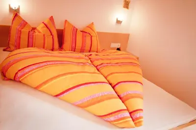 a bed with an orange and yellow striped comforter at Platterhof in Avelengo