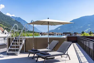 a pair of chairs and an umbrella on a balcony at Villa Hubertus Luxuria Nova Suites - Adults friendly in Naturno