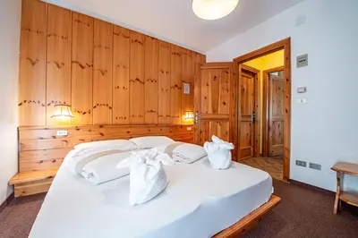 a bedroom with a white bed with wooden walls at Villa Ruggero Wine Hotel in Campitello di Fassa