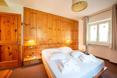 a bedroom with a large white bed with wooden walls at Villa Ruggero Wine Hotel in Campitello di Fassa