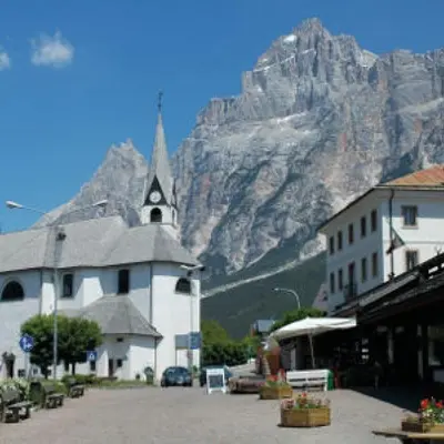 a building with a church with a mountain in the background at Ciasa Coleto in San Vito di Cadore