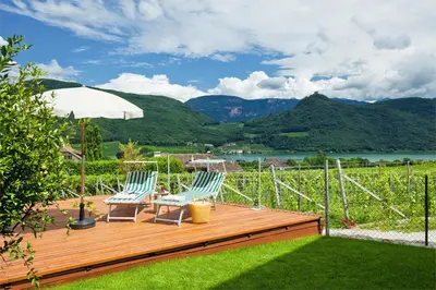 two chairs and an umbrella on a wooden deck at Garni Osannahöfl in Caldaro