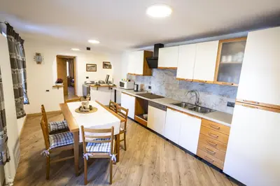 a kitchen with white cabinets and a table and chairs at appartamenti dei Maerins in Pozza di Fassa