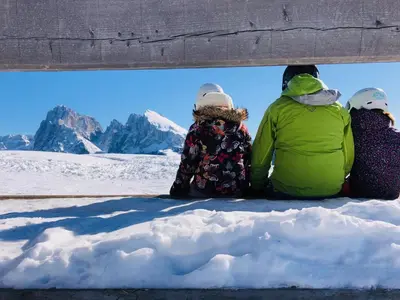 three people sitting on a bench in the snow at Apartments Praverd nelle Dolomiti in Santa Cristina in Val Gardena