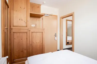 a bedroom with a white bed and a wooden closet at Hotel Euròpa Dolomites in Selva di Val Gardena
