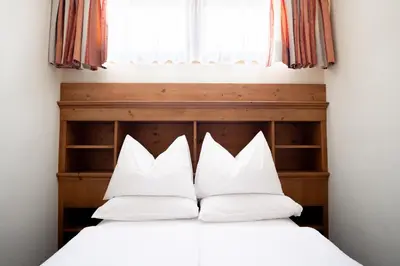 a bedroom with a bed with white sheets and a window at Hotel Euròpa Dolomites in Selva di Val Gardena