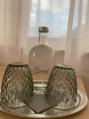 a glass bottle and two glasses on a plate at Hotel Garni Broi - Charme & Relax in Selva di Val Gardena