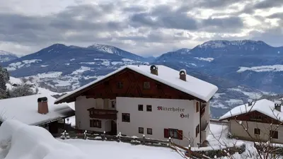 a building in the snow with mountains in the background at Mitterhofer in Villandro