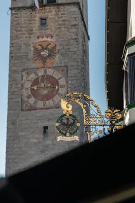 a clock on the side of a brick tower with a clock at Schwarzer Adler - Concept Living in Vipiteno