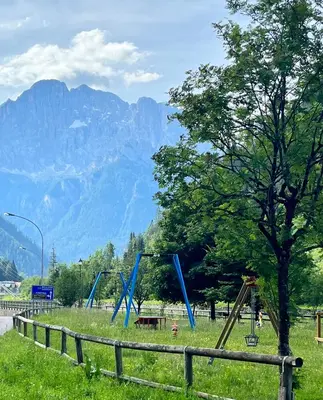 a park with swings and a tree and mountains at Casa di Charme sul Civetta Dolomiti in Caprile