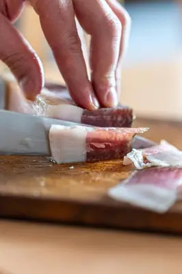 a person cutting meat on a cutting board with a knife at Stampferhof - Agriturismo in Racines