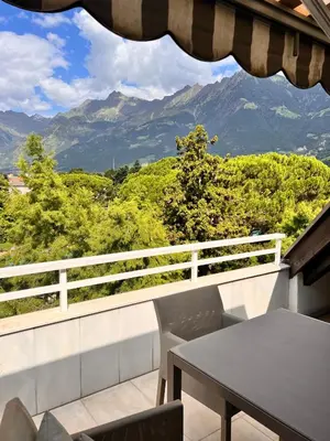 a table and chairs on a balcony with a view of mountains at Penthousetraum im Herzen Merans in Merano