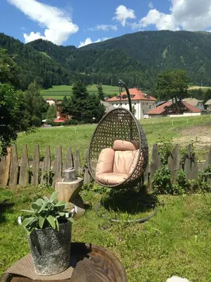 a wicker chair sitting in a field next to a fence at Apartments Resi in Rasùn di Sotto