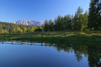 a pond with a fence and mountains in the background at Ferienbauernhof Masunerhof in Fiè