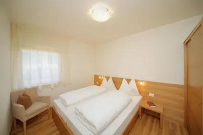 a white bedroom with a bed and a chair at Ferienwohnungen Waldruhe in Santa Valburga St. Walburg