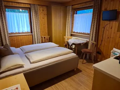 a bedroom with a bed and a table and two windows at Appartement Alpenblick in Valdaora